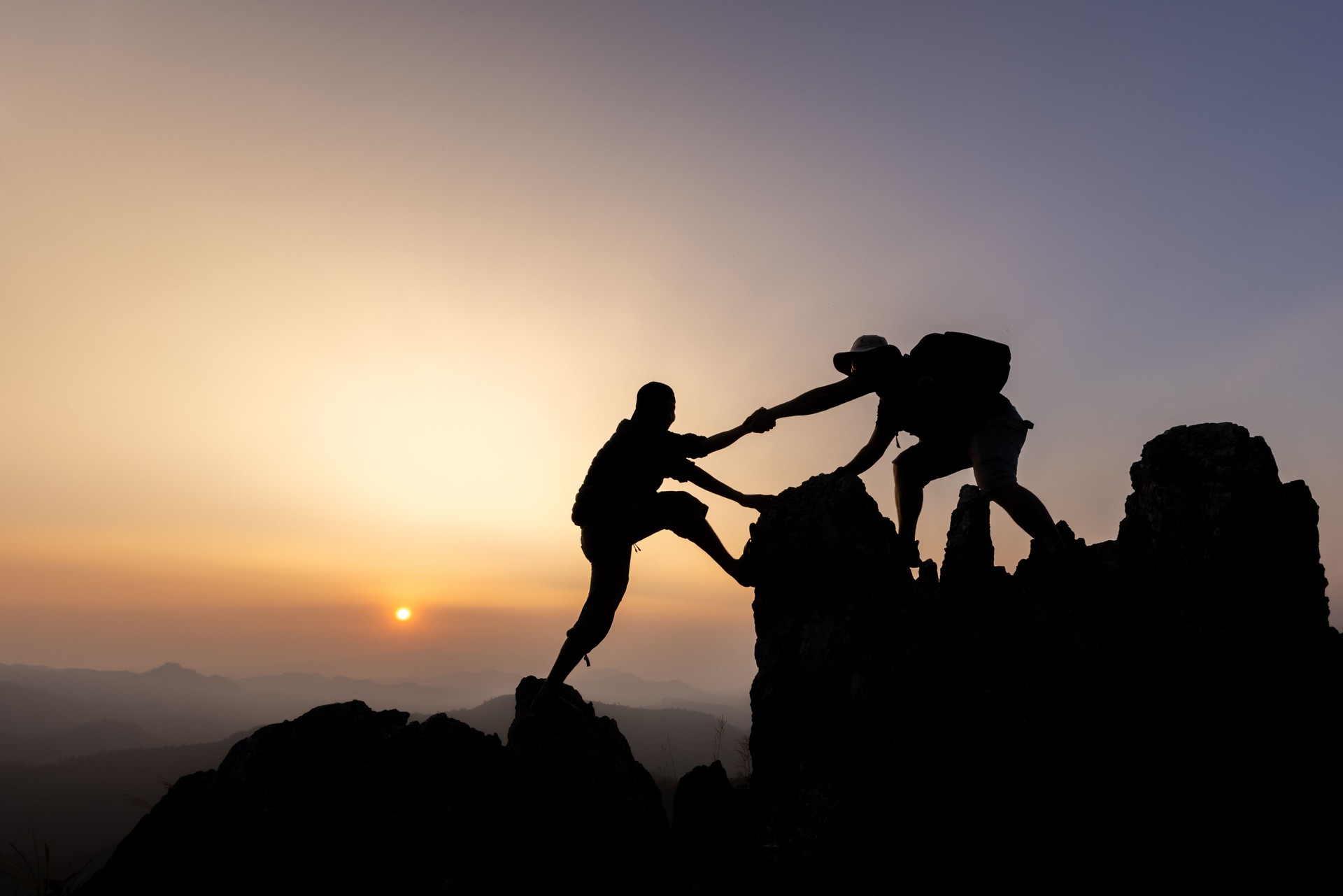Silhouette von Wanderern, die eine Bergklippe hinaufklettern und einer von ihnen hilft. Menschen, die helfen, und Teamwork-Konzept.